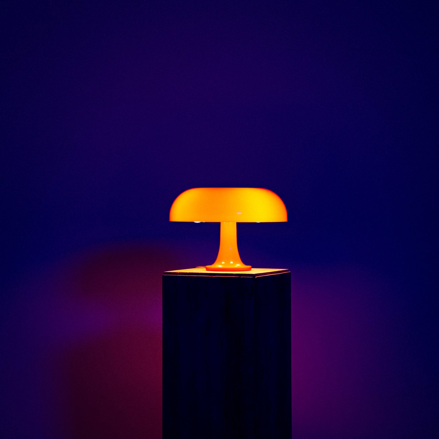 Lumiosa mushroom table lamp with warm orange glow on a pedestal, showcasing iconic Italian design and touch controls.