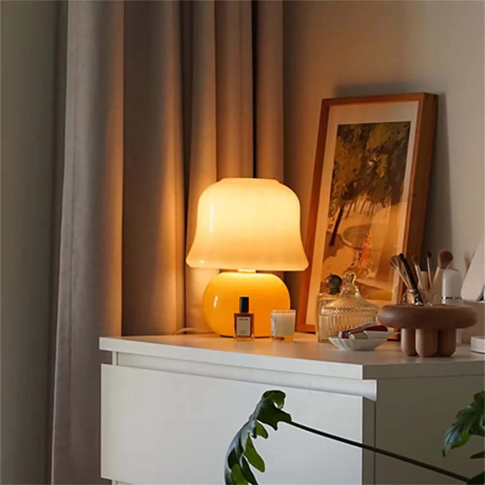 French cream mushroom table lamp providing soft light on a bedside table with decor and curtains in the background.