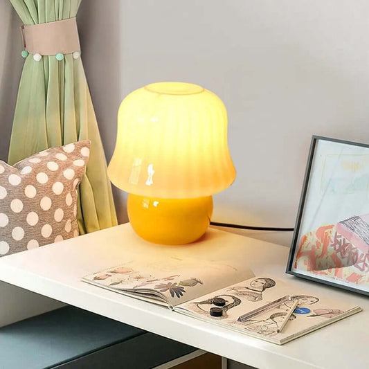 French cream mushroom table lamp with soft yellow light on a bedside table next to decorative items.