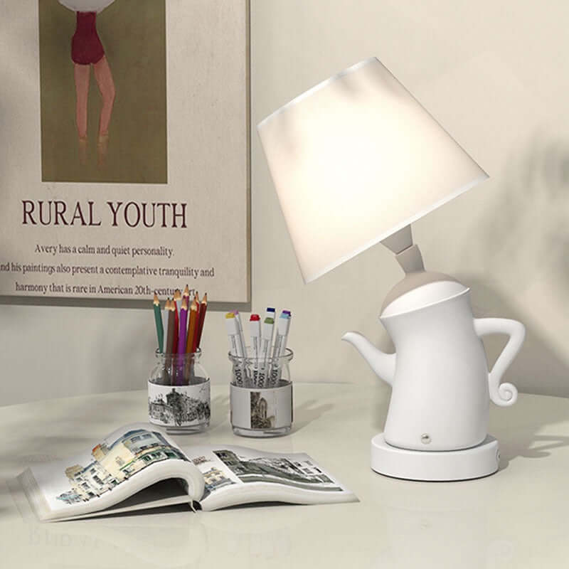 Alice Dream Kettle Lamp on a desk, featuring a whimsical kettle design and a soft lampshade, ideal for ambient lighting.