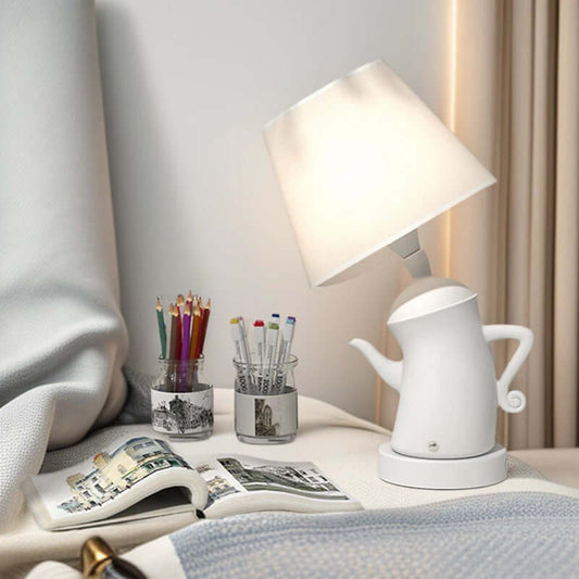 Alice Dream Kettle Lamp illuminating a bedside table with art supplies and a book.