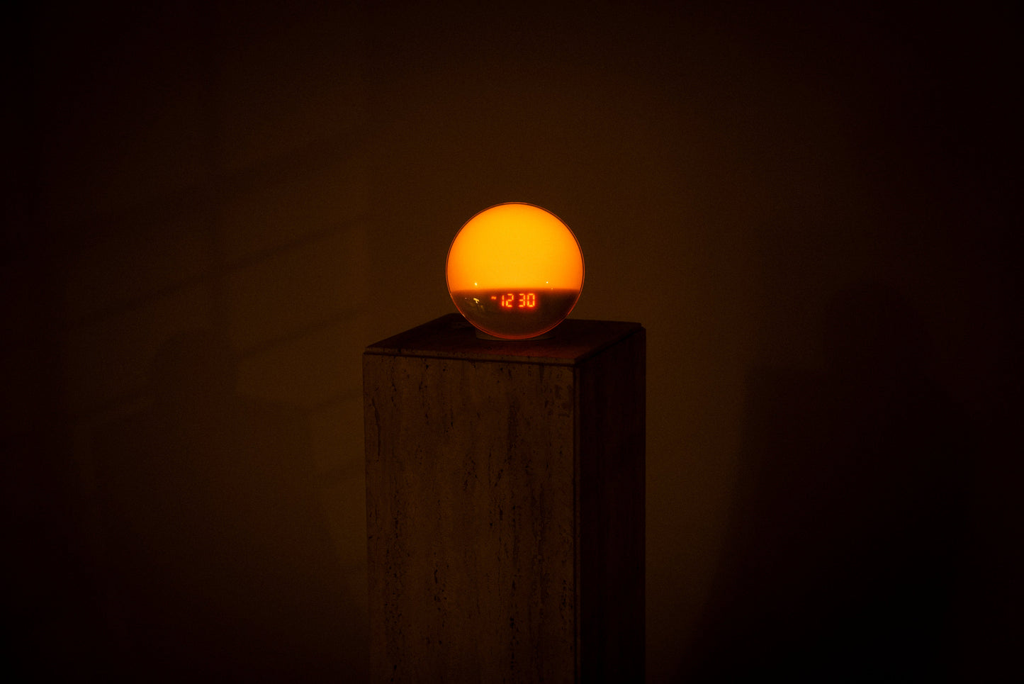 Lumiosa dawn simulator gently waking you with soft light, displayed on a neutral pedestal in a dimly lit room.