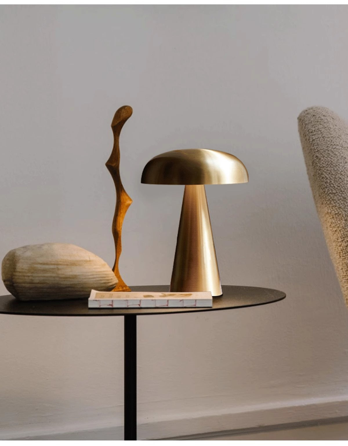 Elegant metal mushroom table lamp on a black side table, accompanied by a decorative stone and sculpture.