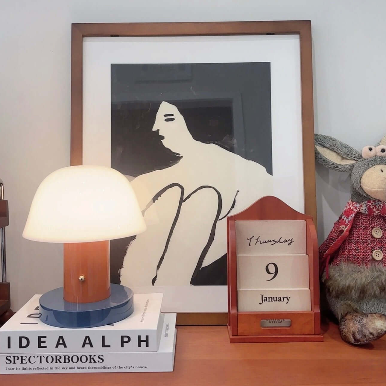 Seta mushroom charging desk lamp next to wall art and a wooden calendar on a stylish desk.