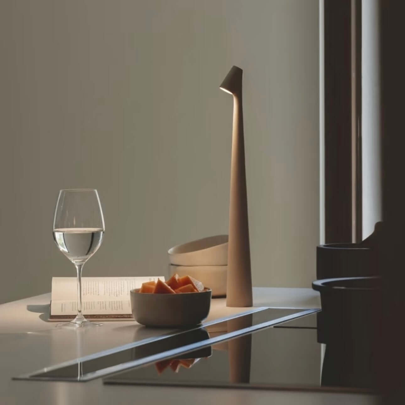 Modern touch-control LED desk lamp on a countertop with a glass of water and a bowl of fruit.