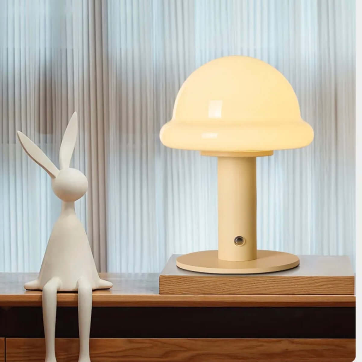 Candy table lamp with soft yellow glow on wooden table next to a white rabbit figurine, adding a cozy touch to the space.