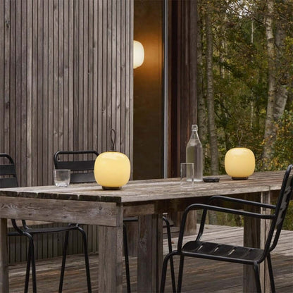 Danish portable table lamps on a wooden outdoor table, creating a cozy ambiance in a nature-inspired setting.