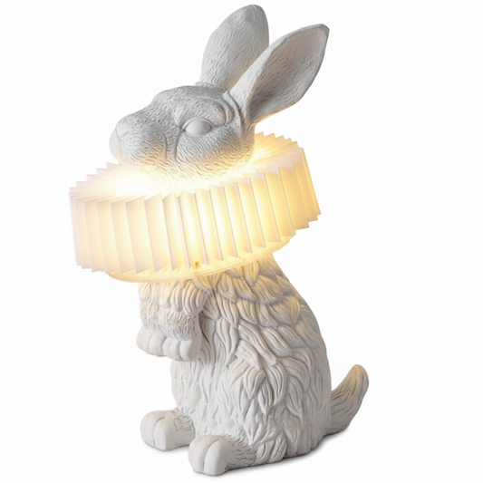 White resin rabbit sculpture table lamp holding glowing ribbed light shade, sitting pose on white background