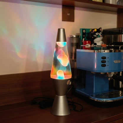Rainbow lava lamp with a brushed metal base and cap, glowing colorful wax, and soft iridescent light on the wall behind it.
