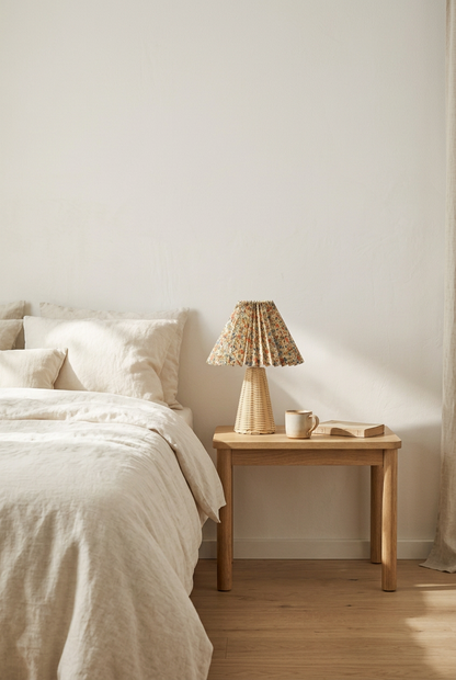 Floral pleated paper table lamp with rattan base on a bedside table