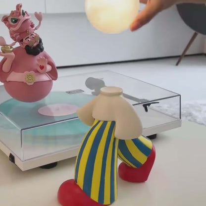 Creative artistic lamp with unique human silhouette beside a colorful figurine on a turntable.